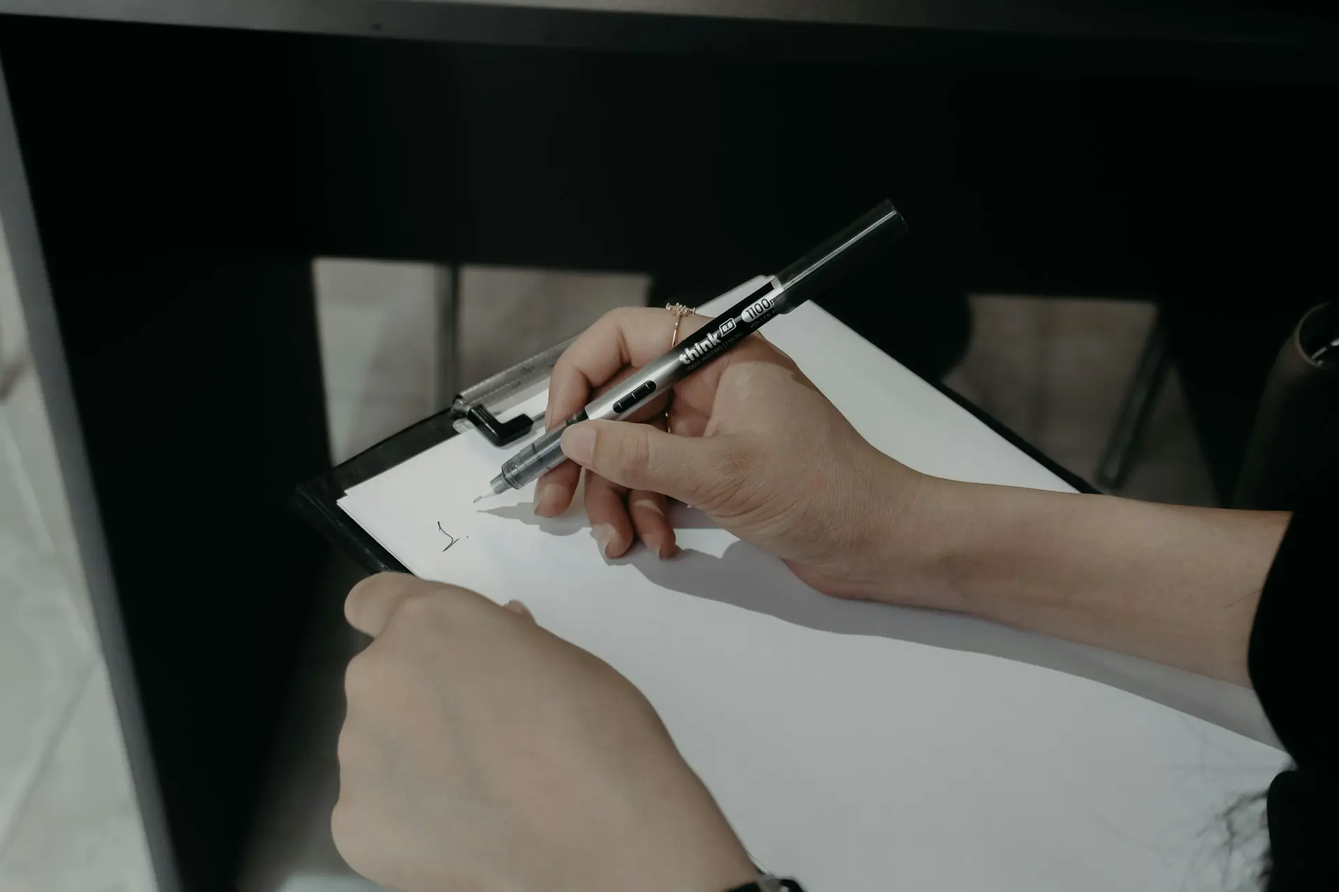 Hands writing on a clipboard with a pen.